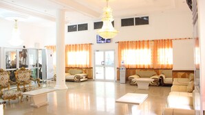 A spacious lobby with a chandelier, seating areas, and a glass wall with a view. - Hôtel Belavie (Bonaberi)