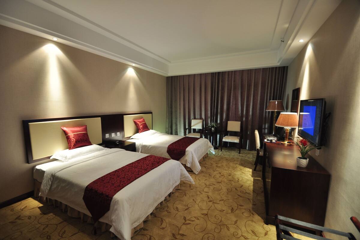 A hotel room with two beds, a desk, a chair, a television, and a large window with curtains.