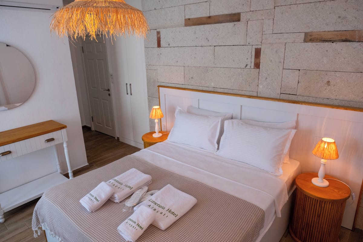 A neatly made bed with white linens and two bedside lamps, a wooden nightstand, and a round mirror on the wall.