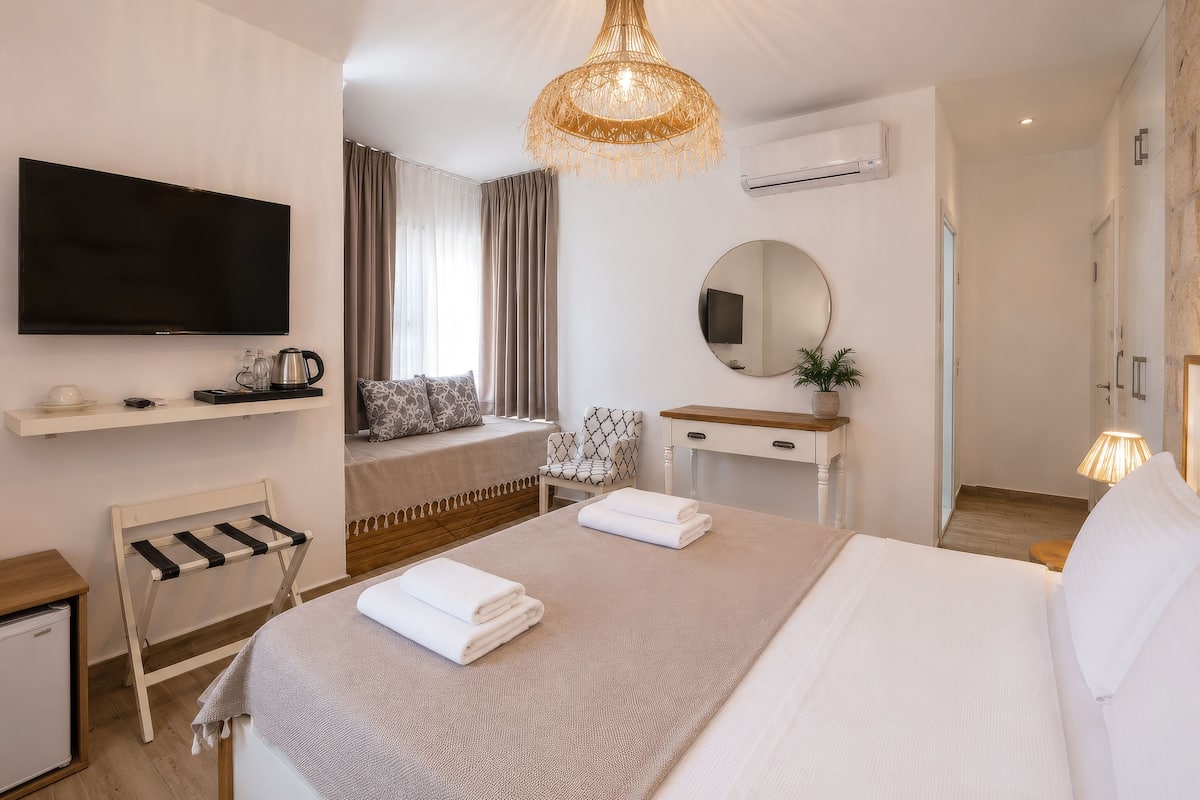 A hotel room with a bed, a TV, a desk, a chair, a mirror, and a hanging light fixture.