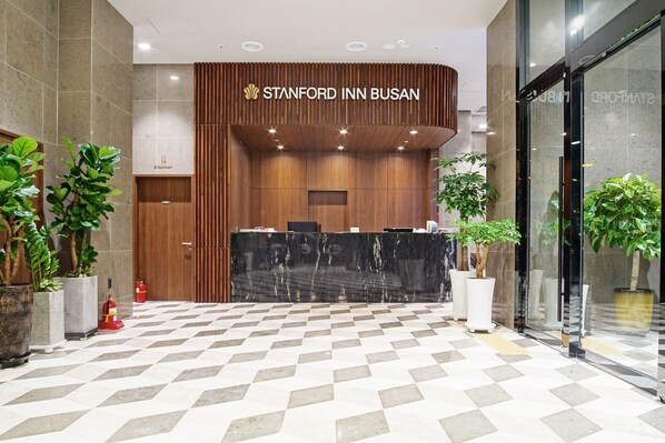 A reception area with a check-in counter, wooden paneling, and potted plants. - Stanford Hotel Busan (Busan)