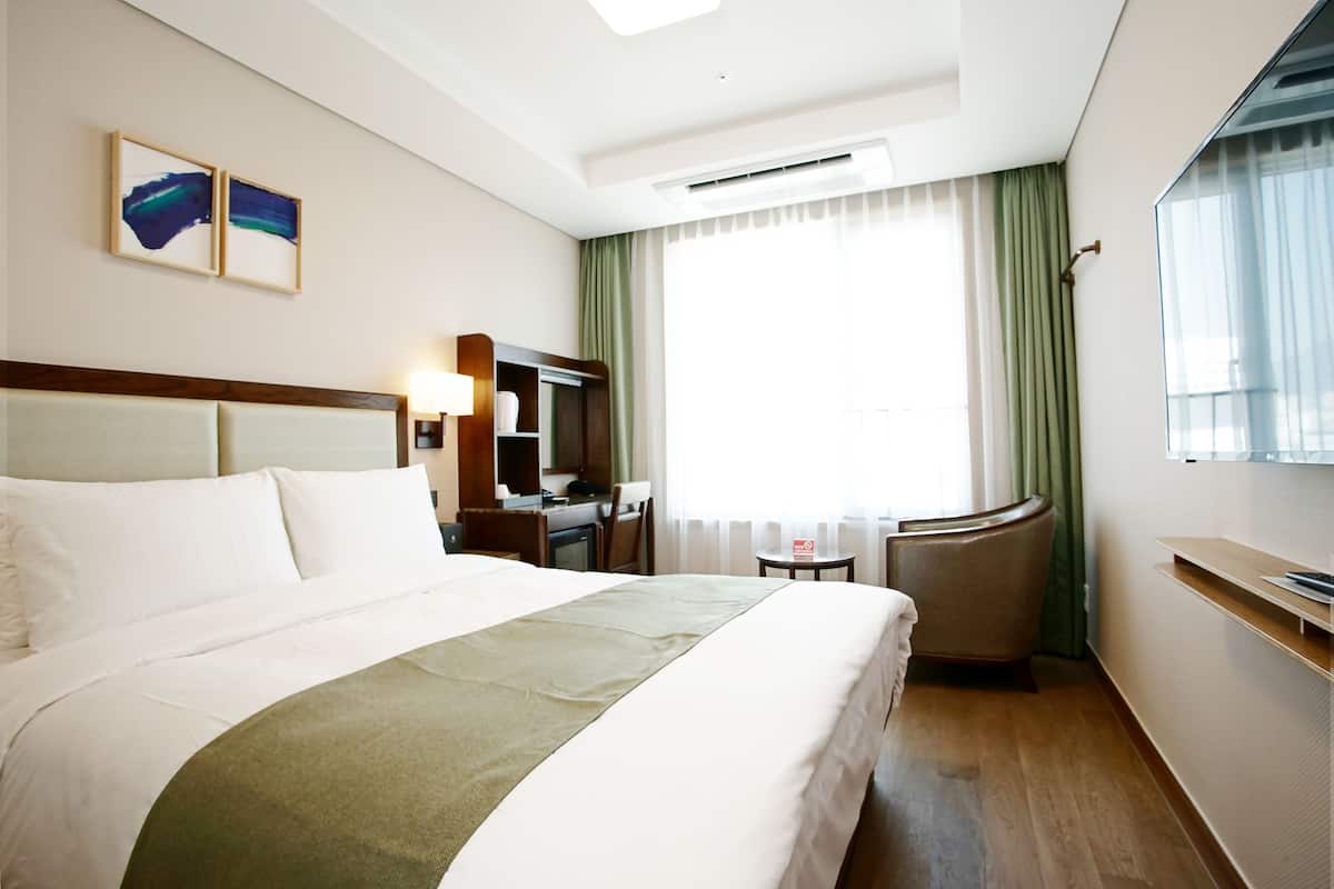 A hotel room with a large bed, a desk, a chair, a small table, and a window with curtains.