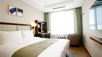 Habitación de hotel con una cama grande, un escritorio, una silla, una mesita y una ventana con cortinas.