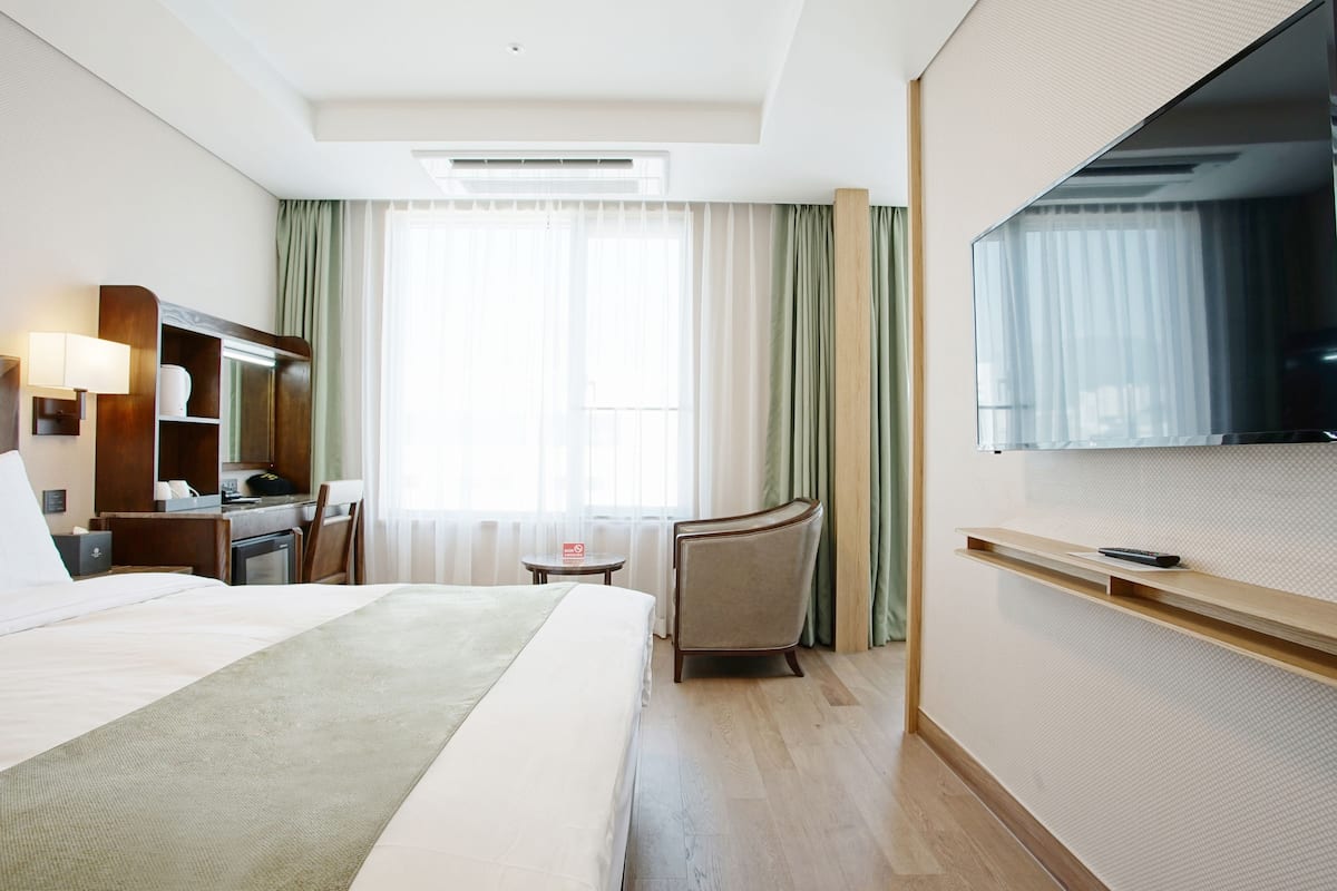 A hotel room with a bed, a desk, a chair, a TV, and a window with curtains.
