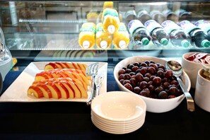 A breakfast buffet with sliced apples, a bowl of grapes, and various juice bottles.