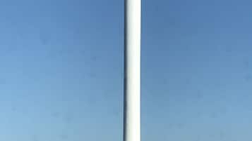 Una torre alta y blanca con un extremo redondeado, rodeada de vegetación y edificios.