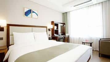 A hotel room with a large bed, a desk, a chair, a small table, a mirror, and a window with curtains.