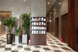 Un vestíbulo con piso a cuadros, una estantería con folletos y plantas en macetas.