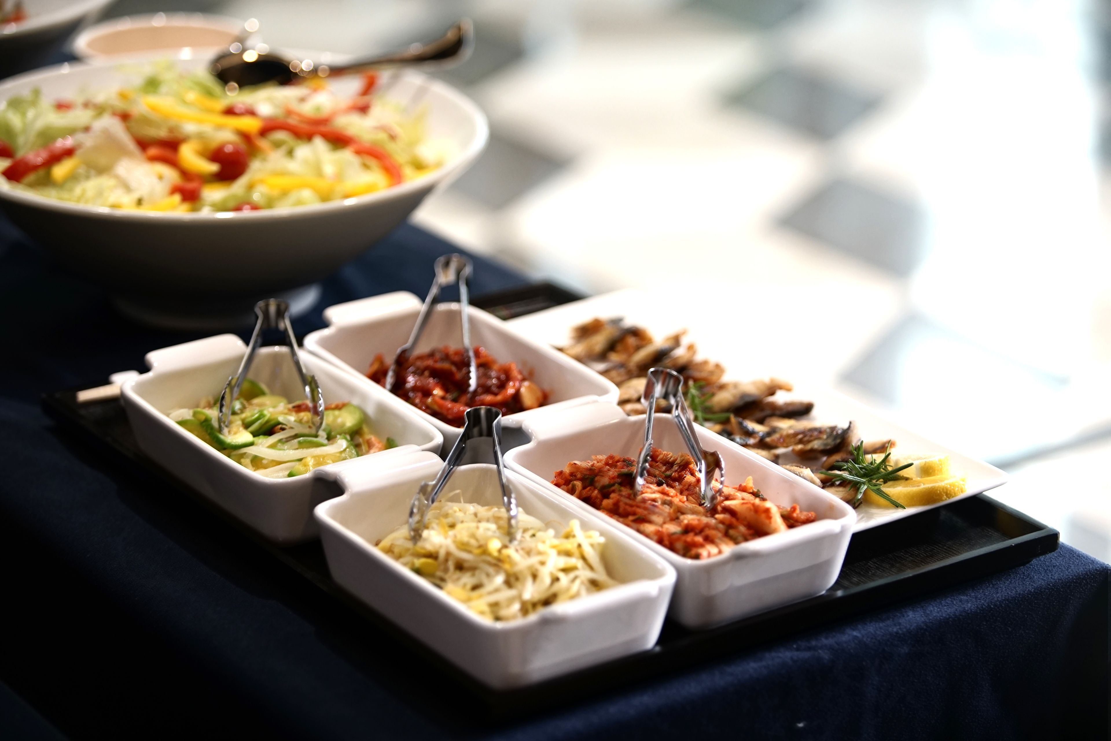 A buffet table with various food items in white trays, including salads, vegetables, and meats.