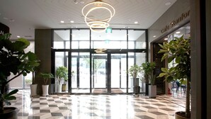 Eine Hotelhalle mit Schachbrettmuster-Bodenbelag, großen Topfpflanzen und einer modernen Deckenleuchte.