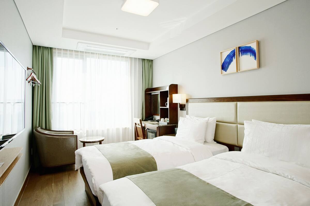 A hotel room with two beds, a desk, a chair, a mirror, and a window with curtains.