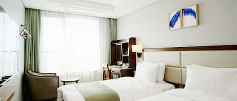 Habitación de hotel con dos camas, un escritorio, una silla, un espejo y una ventana con cortinas.