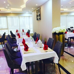 Formal dining area with tables set for a sophisticated meal, featuring comfortable chairs and a large window.