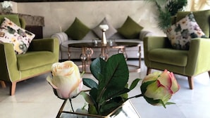 Un hall d’entrée avec des canapés verts, une table basse et un vase rempli de roses.