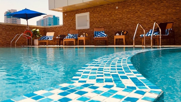 Une piscine aux carreaux de mosaïque bleus et blancs, des chaises longues et un parasol bleu.