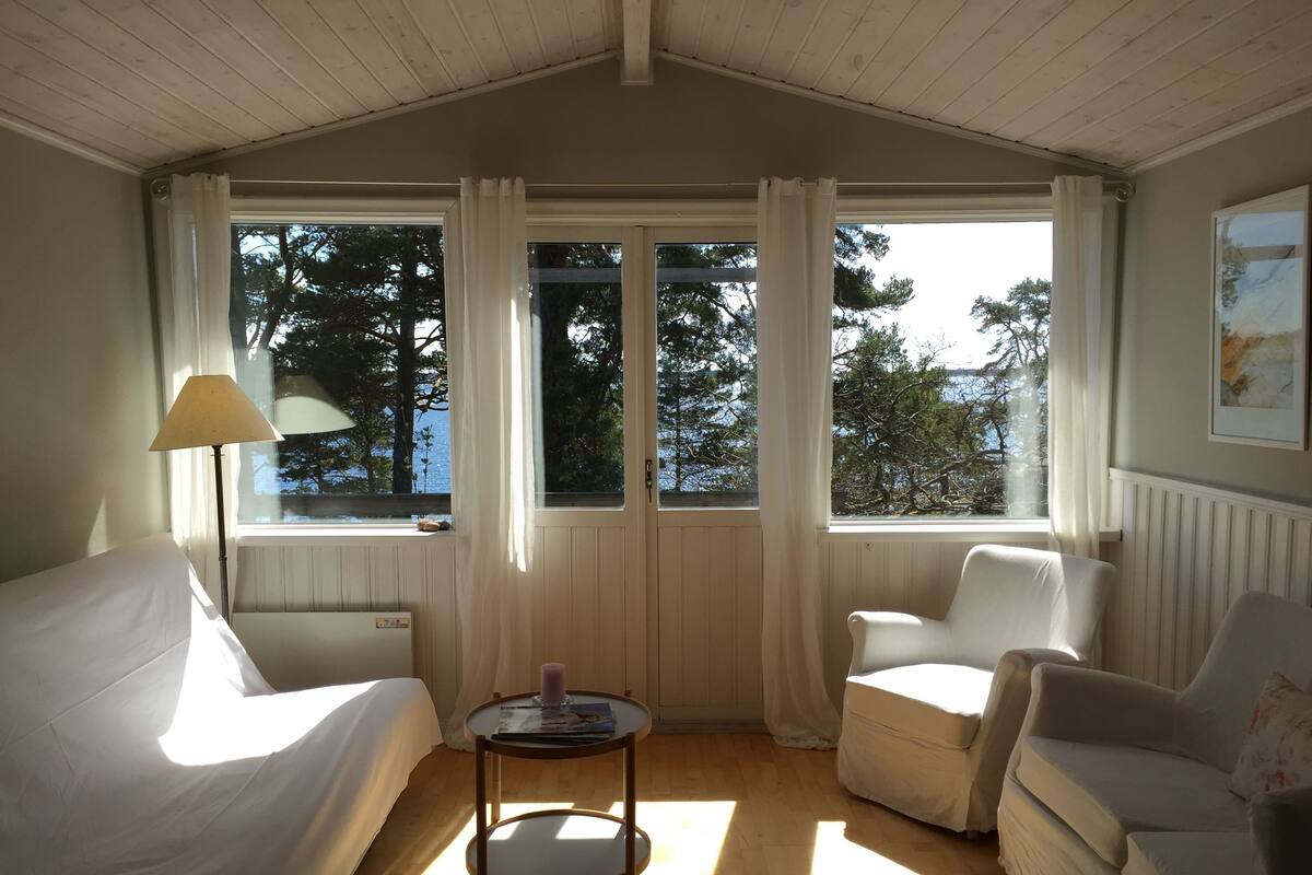 Ein gemütliches Zimmer mit einem Bett, zwei Stühlen, einem kleinen Tisch und großen, mit Vorhängen versehenen Fenstern.