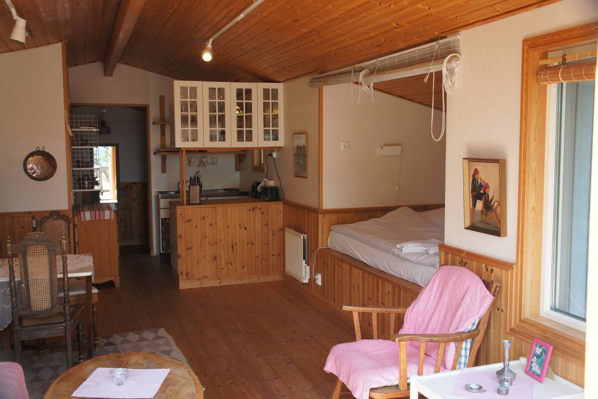 Ein gemütliches Blockhaus mit Essbereich aus Holz, einer Küche, einem Schlafzimmer mit Etagenbett und einem großen Fenster.