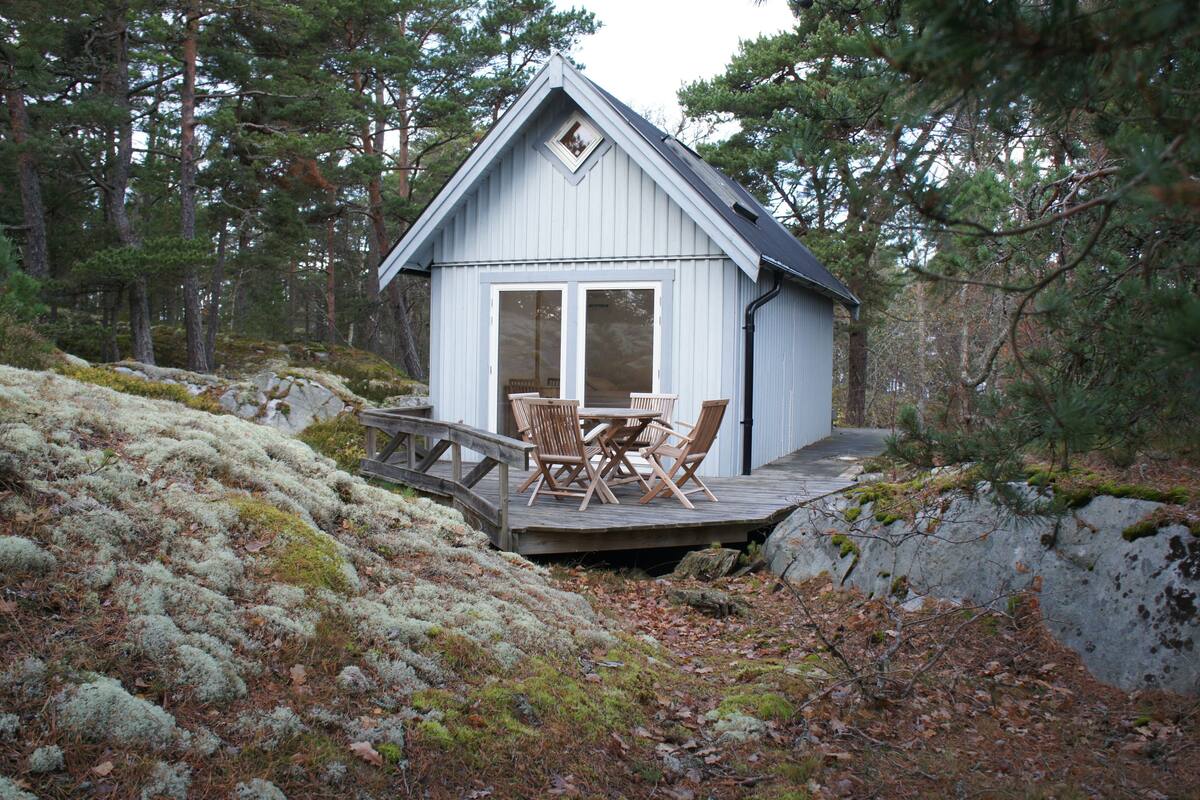 Eine kleine Holzhütte mit einer Veranda und Sitzgelegenheit im Freien, umgeben von Wald.