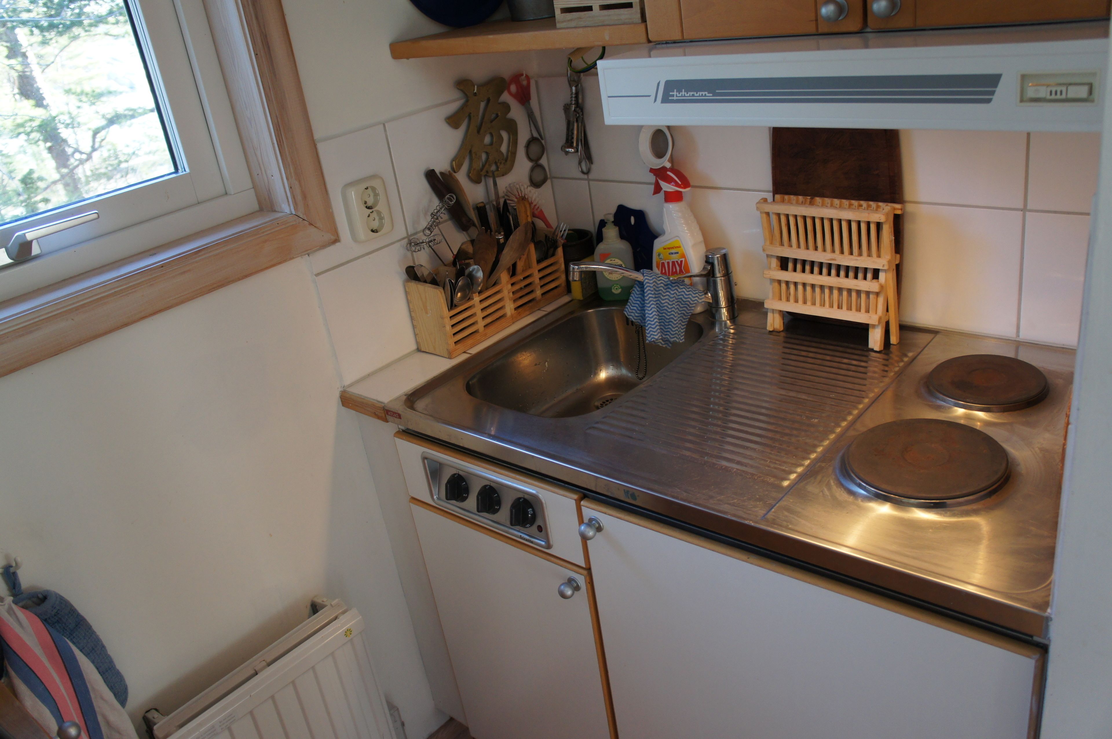 A compact kitchen with a sink, stove, and wooden utensil holder.