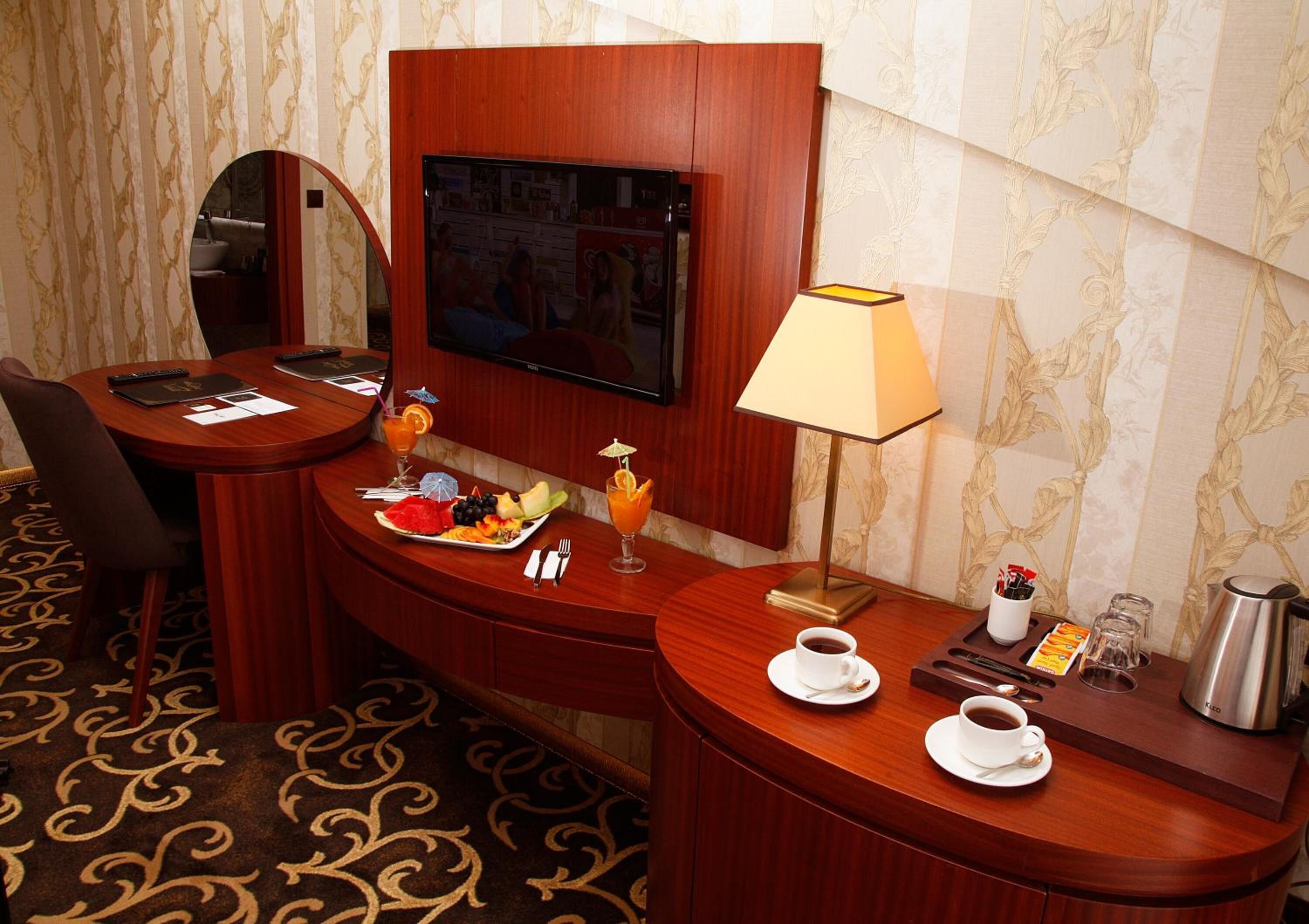 Une chambre d’hôtel avec un bureau en bois, une télévision, une lampe, une machine à café et une assiette de fruits.