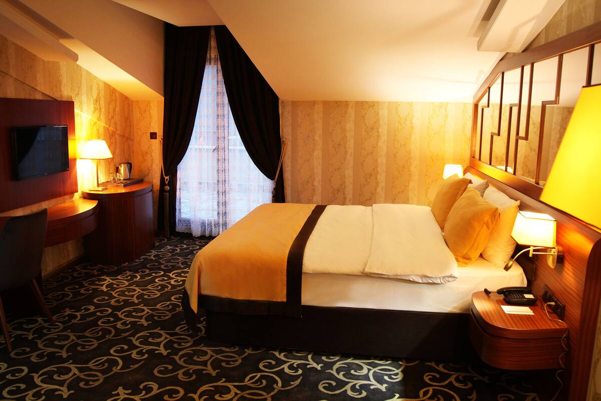 A hotel room with a bed, a desk, a television, and a window with curtains.