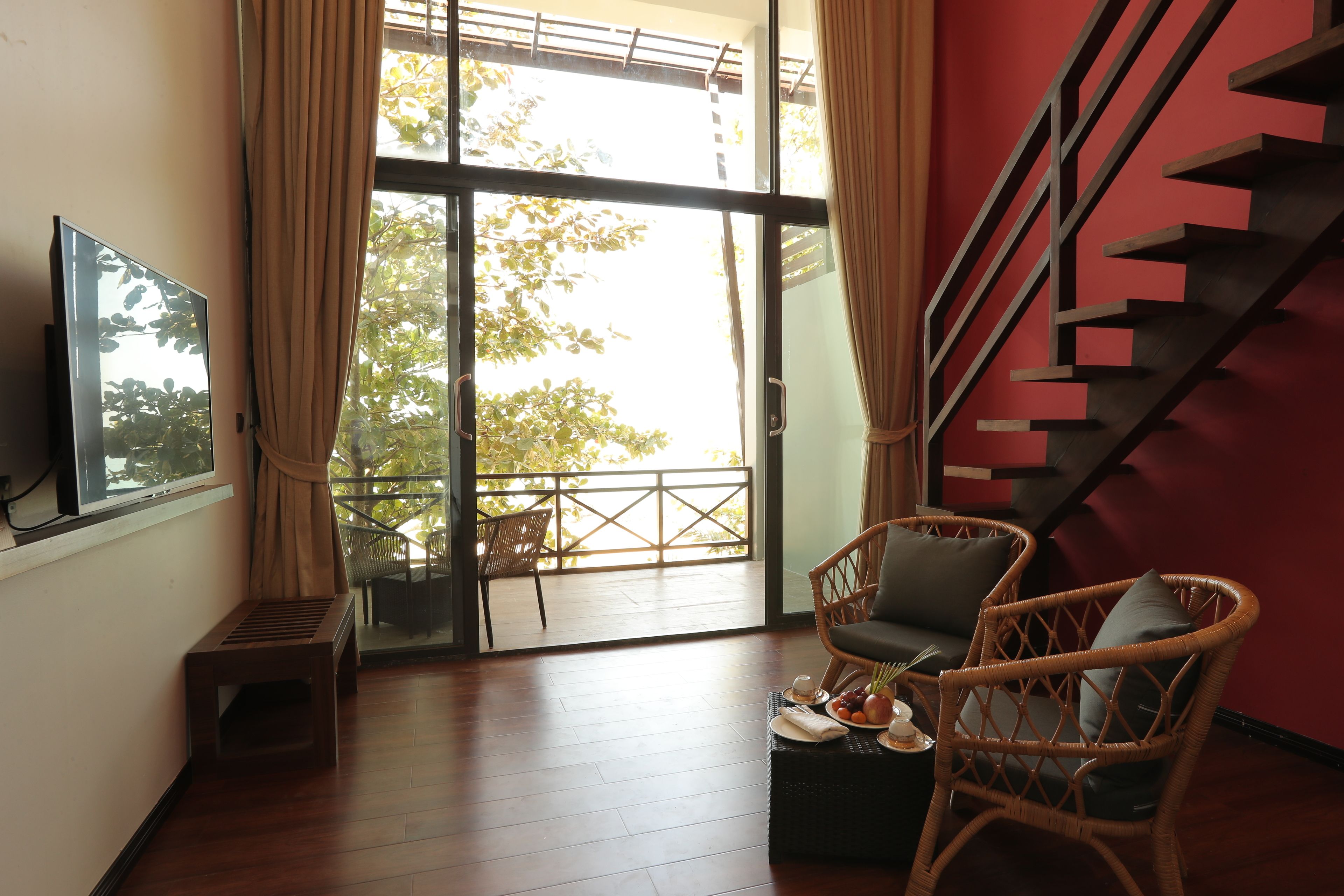 Una habitación con un gran ventanal, una escalera, muebles de mimbre y una pequeña mesa con un plato de comida.
