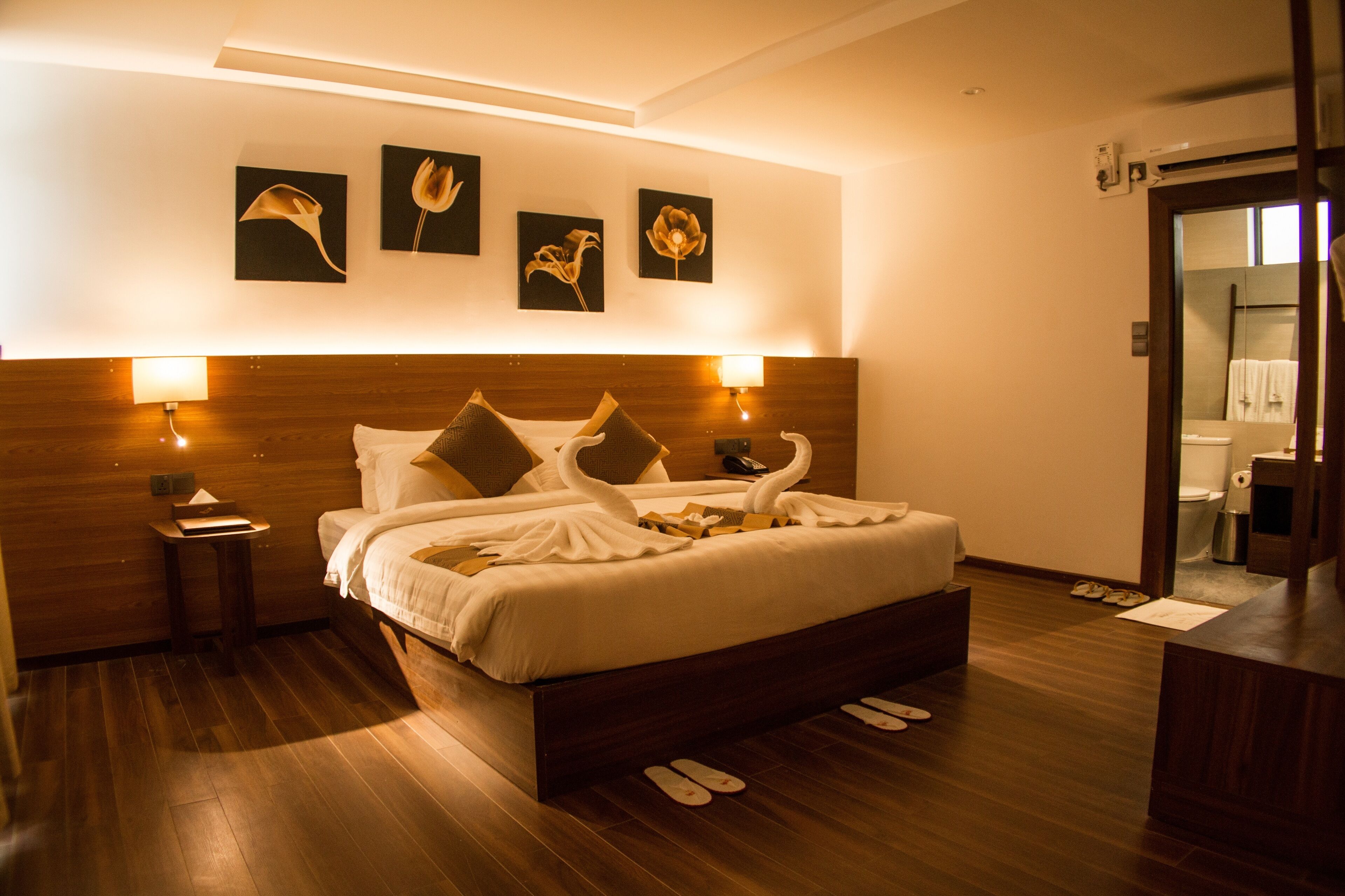 Habitación de hotel con una cama grande, cabecero de madera, una obra de arte colgada en la pared y piso de madera.