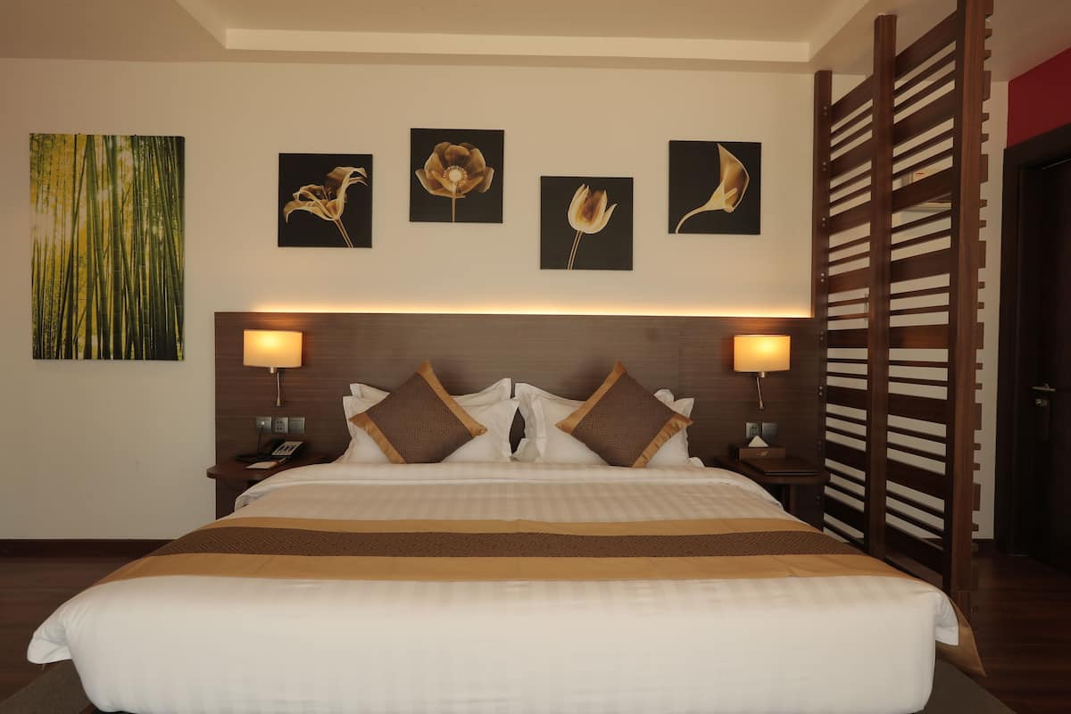Quarto de hotel com uma cama grande, duas mesas de cabeceira, um painel de cabeceira de madeira e obras de arte nas paredes.
