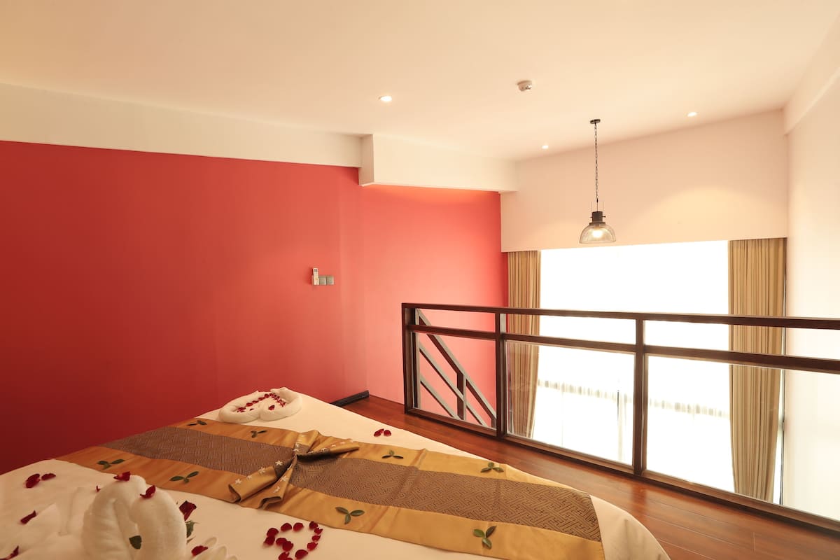 Quarto de hotel com cama, janela com cortinas, varanda com guarda-corpo e luminária suspensa.