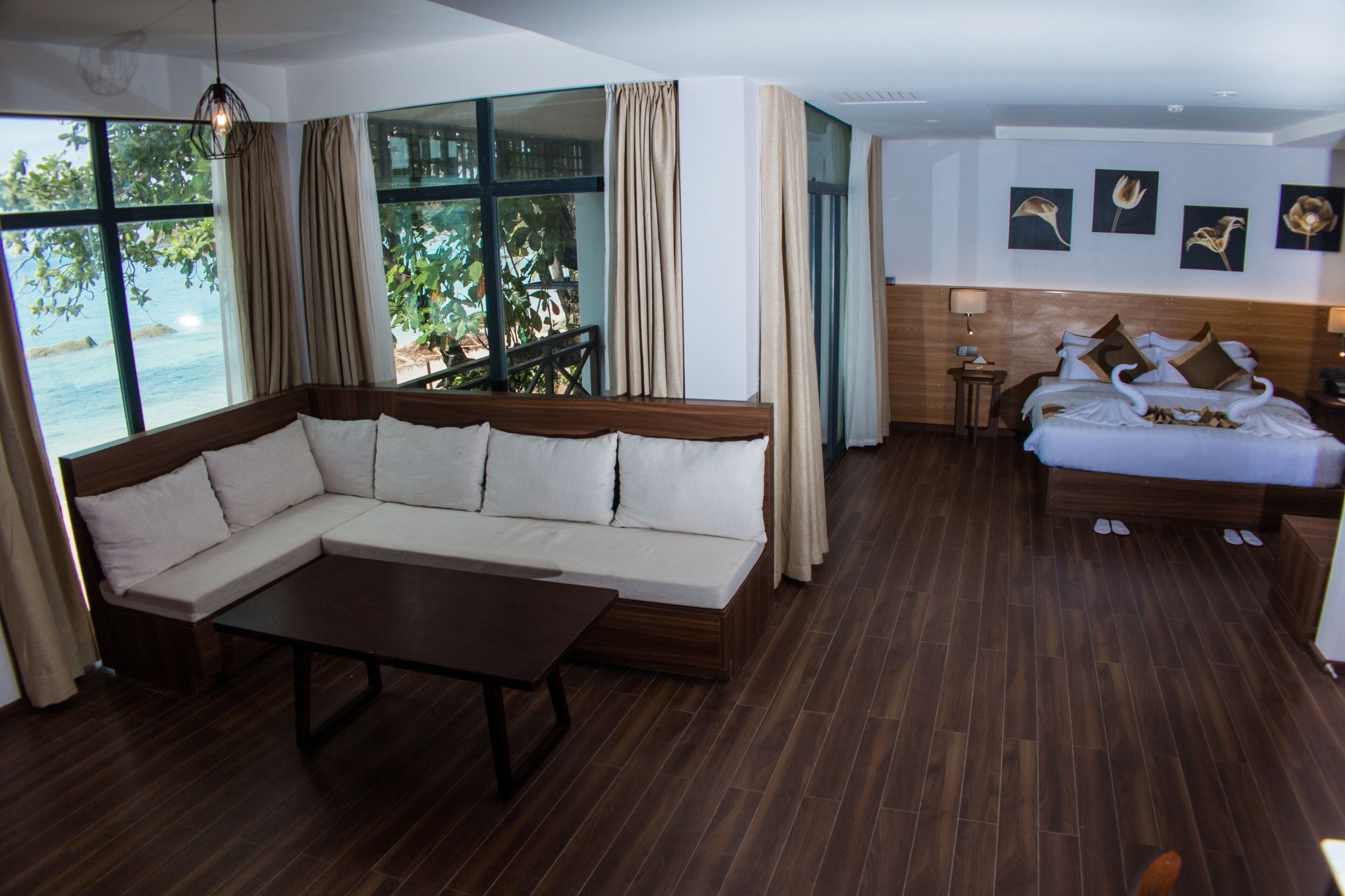 A modern hotel room with a large window, a sofa, a bed, and a wooden floor.