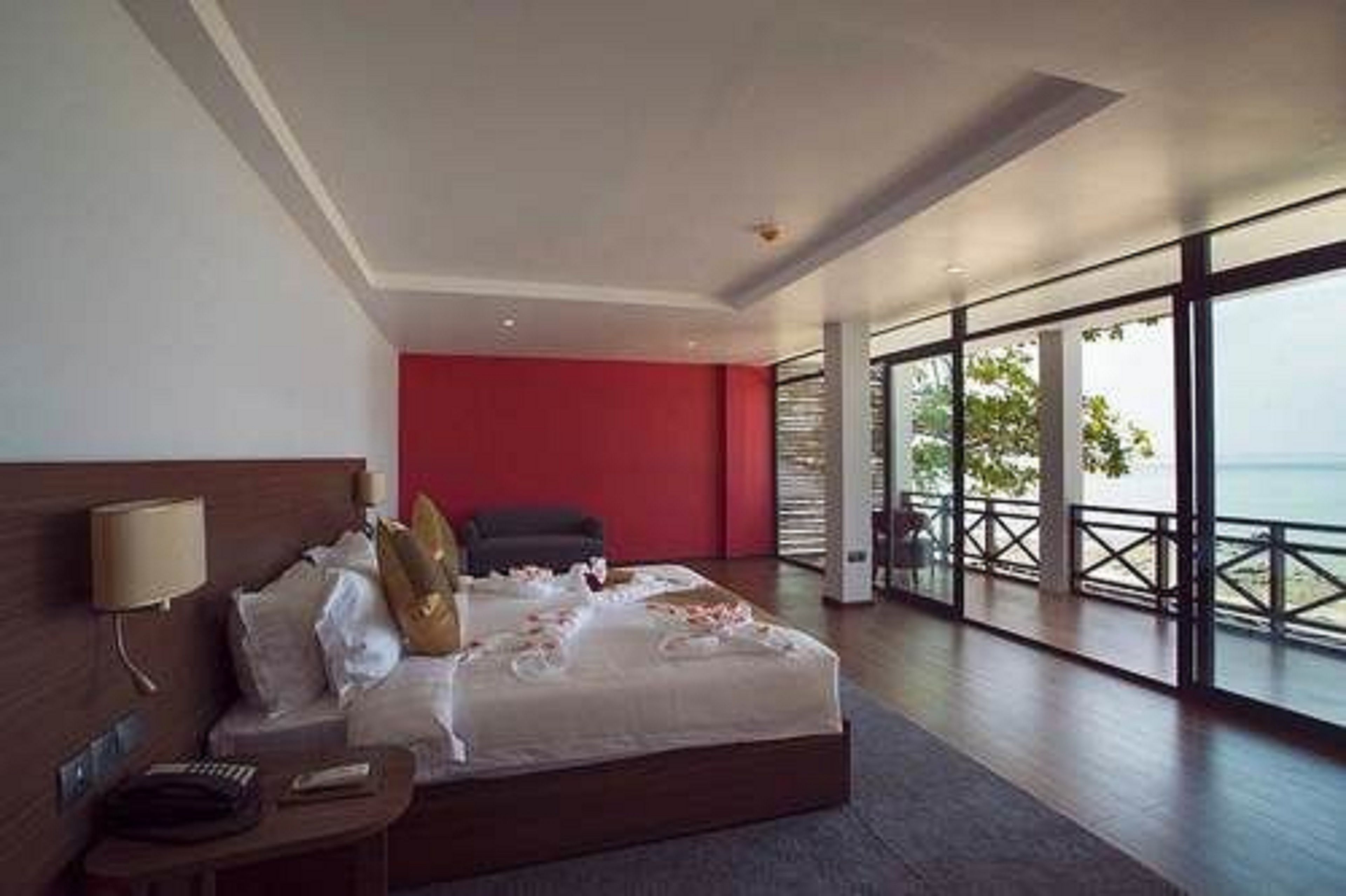 Una habitación de hotel moderna con una cama grande, una mesita de noche y vistas al mar a través de amplias ventanas.