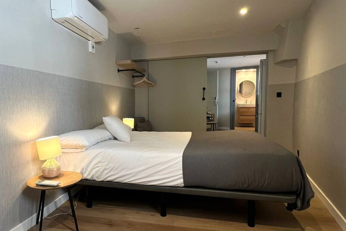 Ein modernes Schlafzimmer mit einem Einzelbett, Nachttischen, einer Wand-Klimaanlage und einem Flur zum Badezimmer.