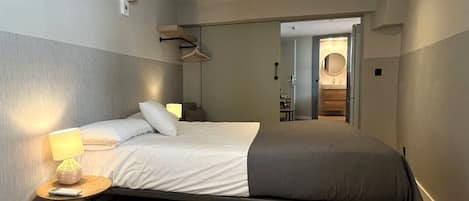 A modern bedroom with a single bed, bedside tables, a wall-mounted air conditioner, and a hallway leading to a bathroom.