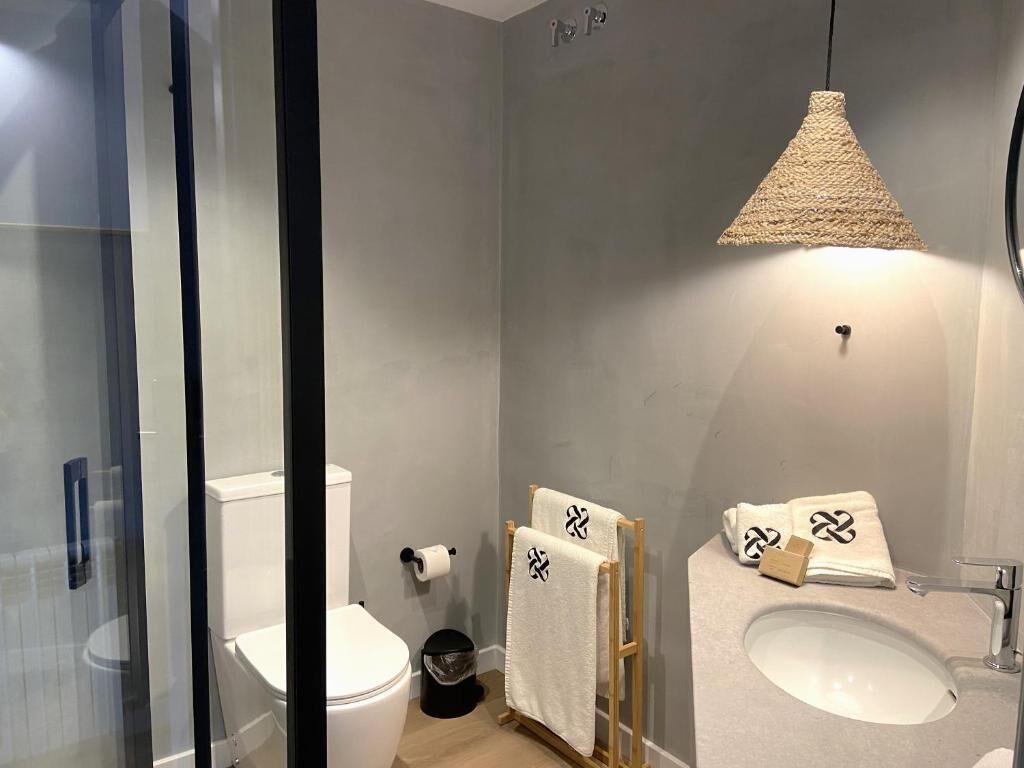 Un baño moderno con cabina de ducha de vidrio, inodoro, lavabo y una lámpara colgante.