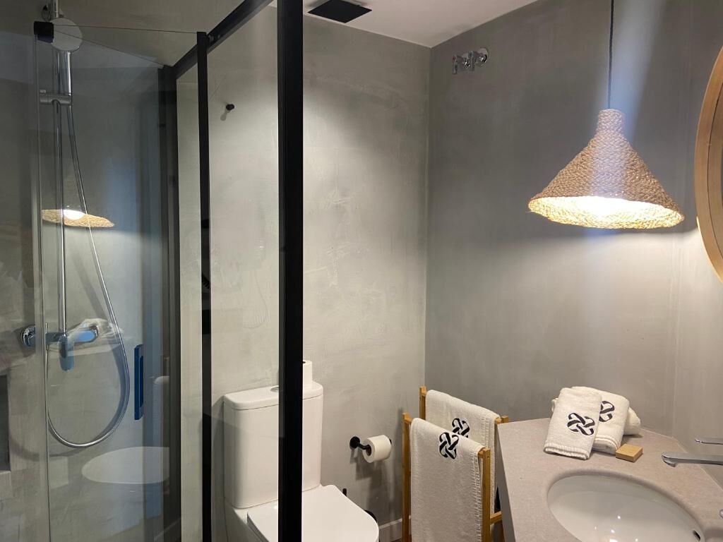 Ein modernes Badezimmer mit einer Duschkabine aus Glas, einer Toilette, einem Waschbecken und einer Pendelleuchte.