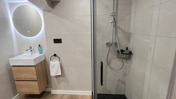 Een moderne badkamer met een douchecabine van glas, een ronde spiegel, een houten wastafelmeubel en een witte handdoek.