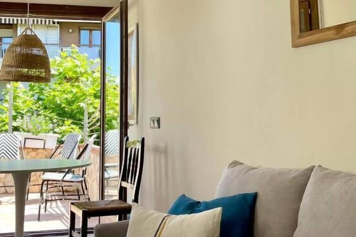 Ein Wohnzimmer mit einer Couch, einem Esstisch und Stühlen. Blick auf einen Balkon mit Pflanzen und einer Pendelleuchte.