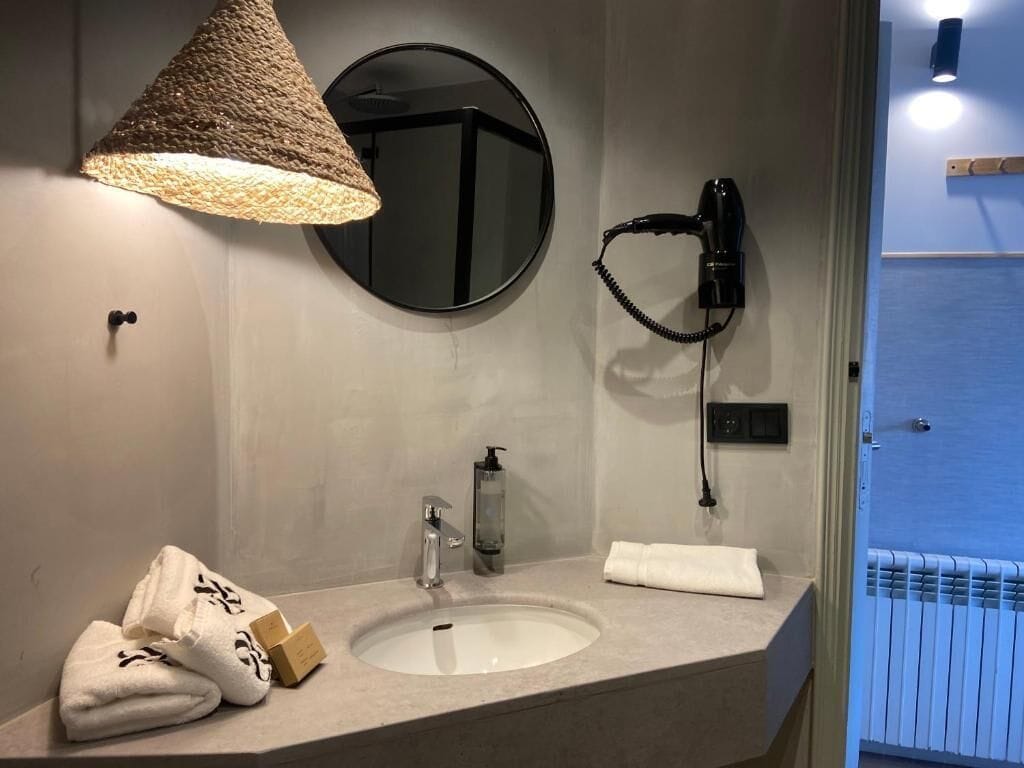 A bathroom with a round mirror, a sink, a towel rack, and a hairdryer.