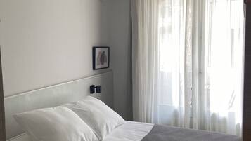 Una cama bien tendida con sábanas blancas, un plaid gris y un cabecero con iluminación empotrada.