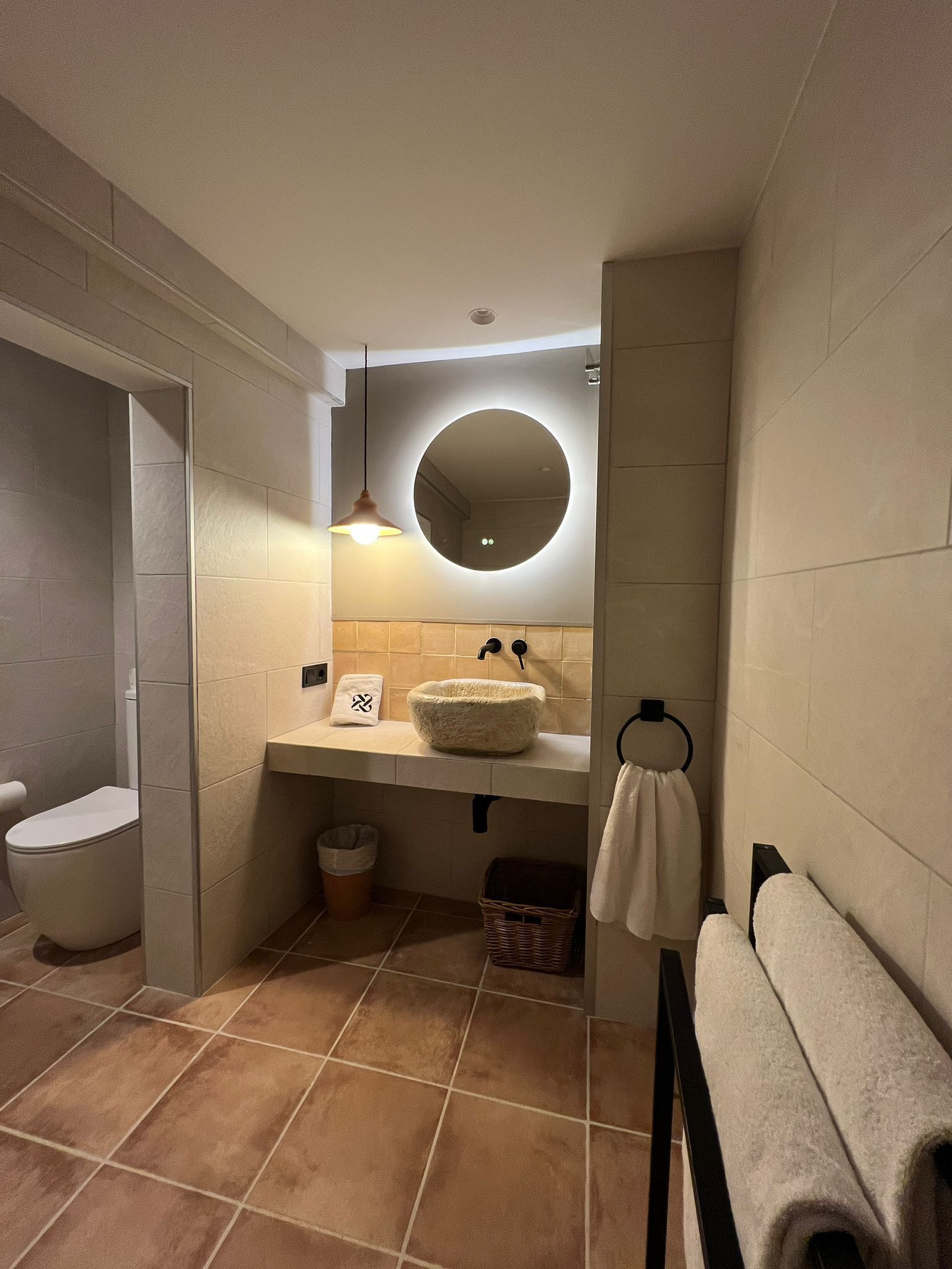 A modern bathroom with a round mirror, a white sink, and a toilet.