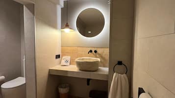 A modern bathroom with a round mirror, a white sink, and a toilet.