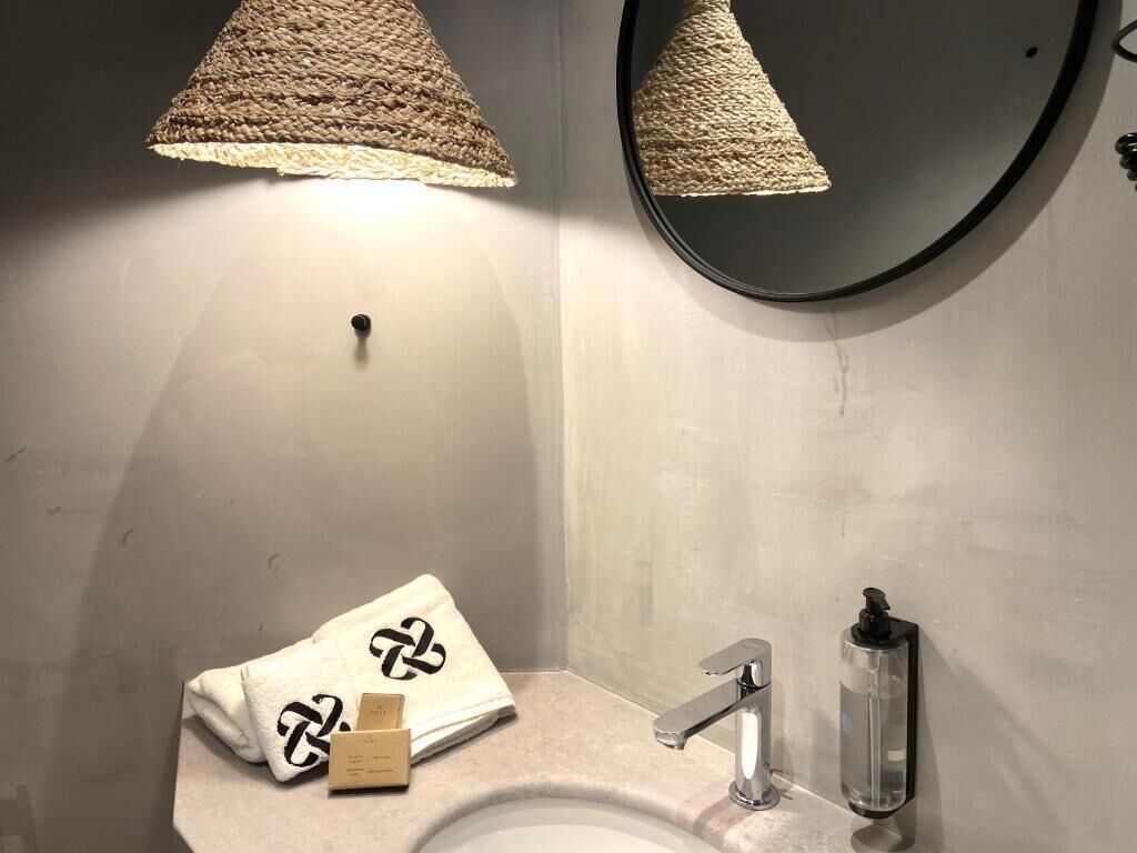 A bathroom with a round mirror, a sink with a modern faucet, and a towel with a logo.