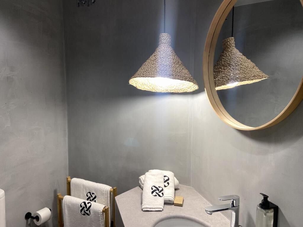 A modern bathroom with a round mirror, two hanging lamps, a sink, and two towels with a logo.
