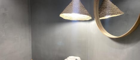 A modern bathroom with a round mirror, two hanging lamps, a sink, and two towels with a logo.