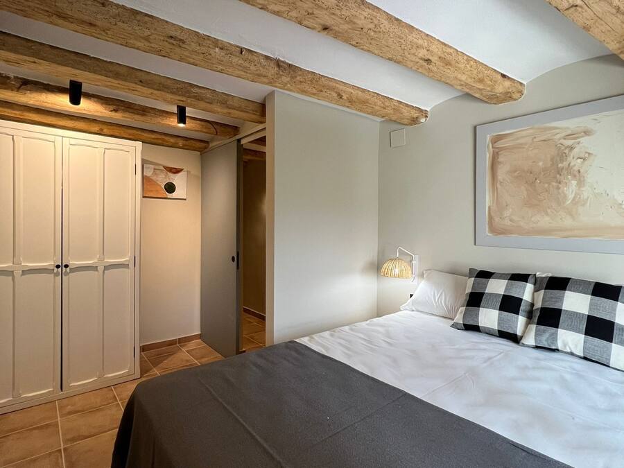 A bedroom with a bed, checkered pillows, a wall-mounted lamp, and a painting.