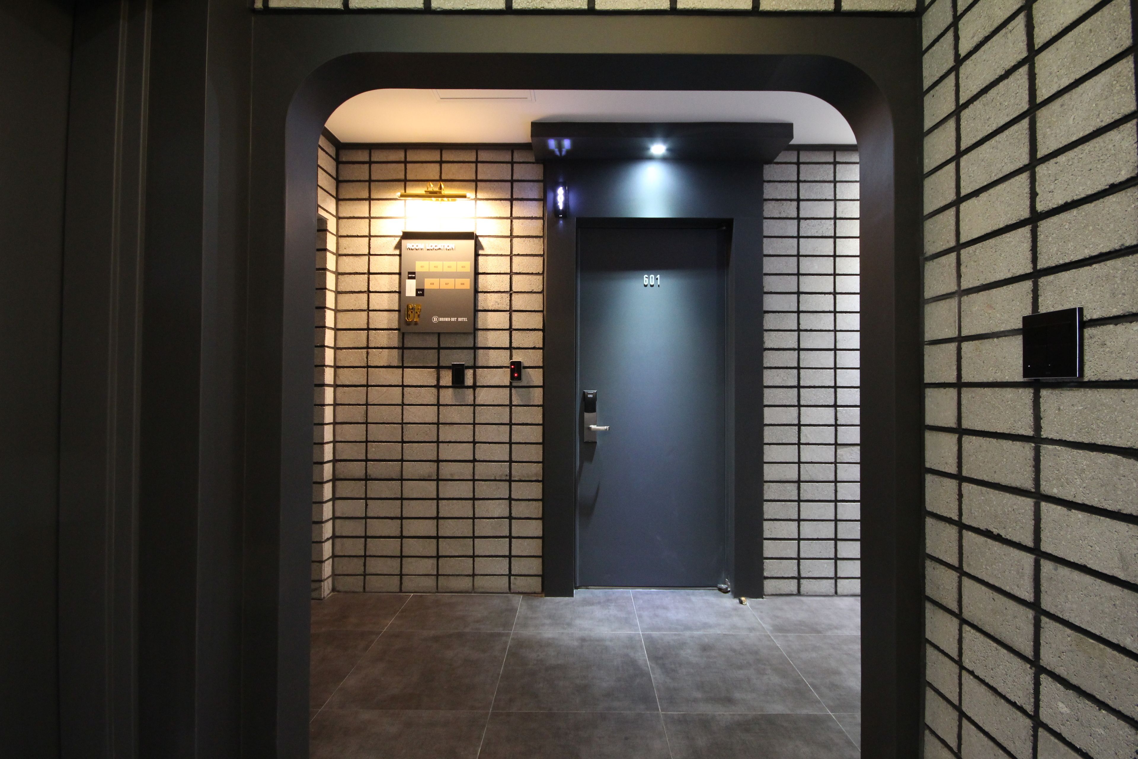 Um elevador moderno com painel digital, parede revestida de azulejos e porta escura.