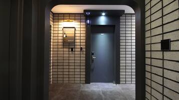 Um elevador moderno com painel digital, parede revestida de azulejos e porta escura.