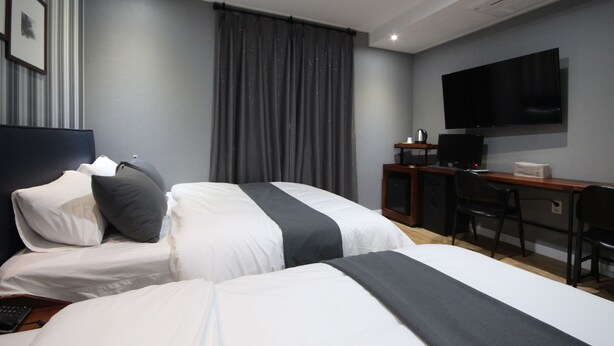 A hotel room with two beds, a desk, a chair, a television, and a curtain.