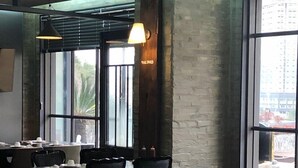 A restaurant interior with high windows, exposed brick walls, and modern furniture.
