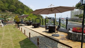 An outdoor seating area with tables and umbrellas, surrounded by a wooden deck and gravel path.